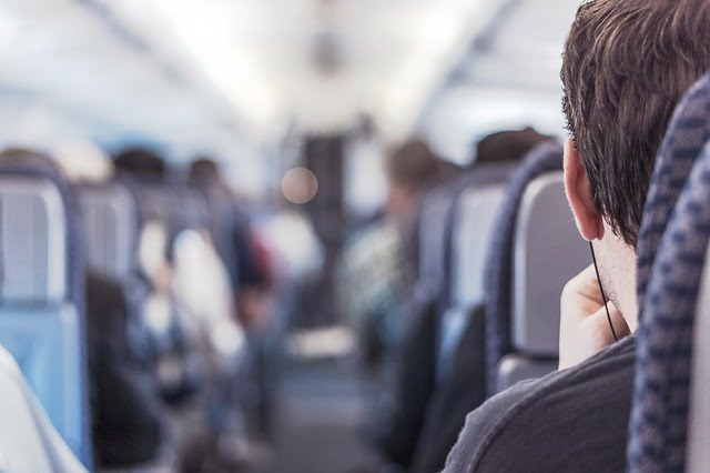 The back of a young man sitting at the rear of the train. The train is fairly full with other passengers.