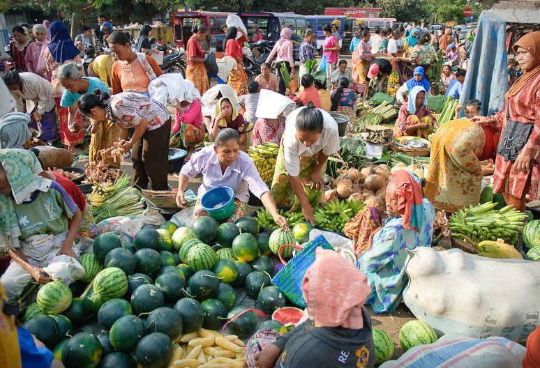 Image shows a busy Indonesian market  with people buying fruit and vegetables