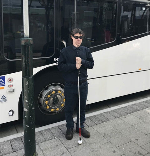 Man holding a mobility cane at a bus stop