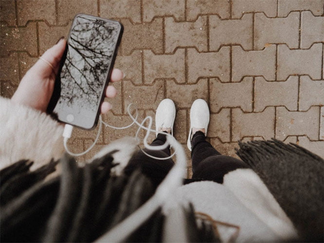 A birds eye view image of a person holding a phone with headphones plugged in.